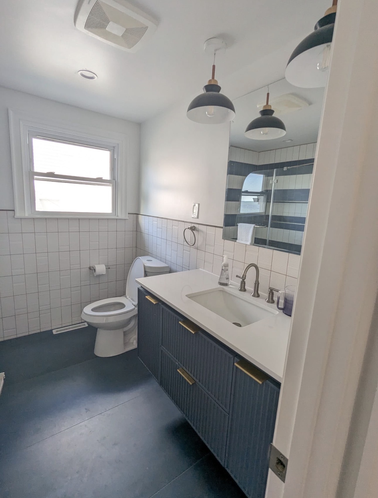 Remodeled bathroom with navy vanity, white tile wainscot and pendant lights
