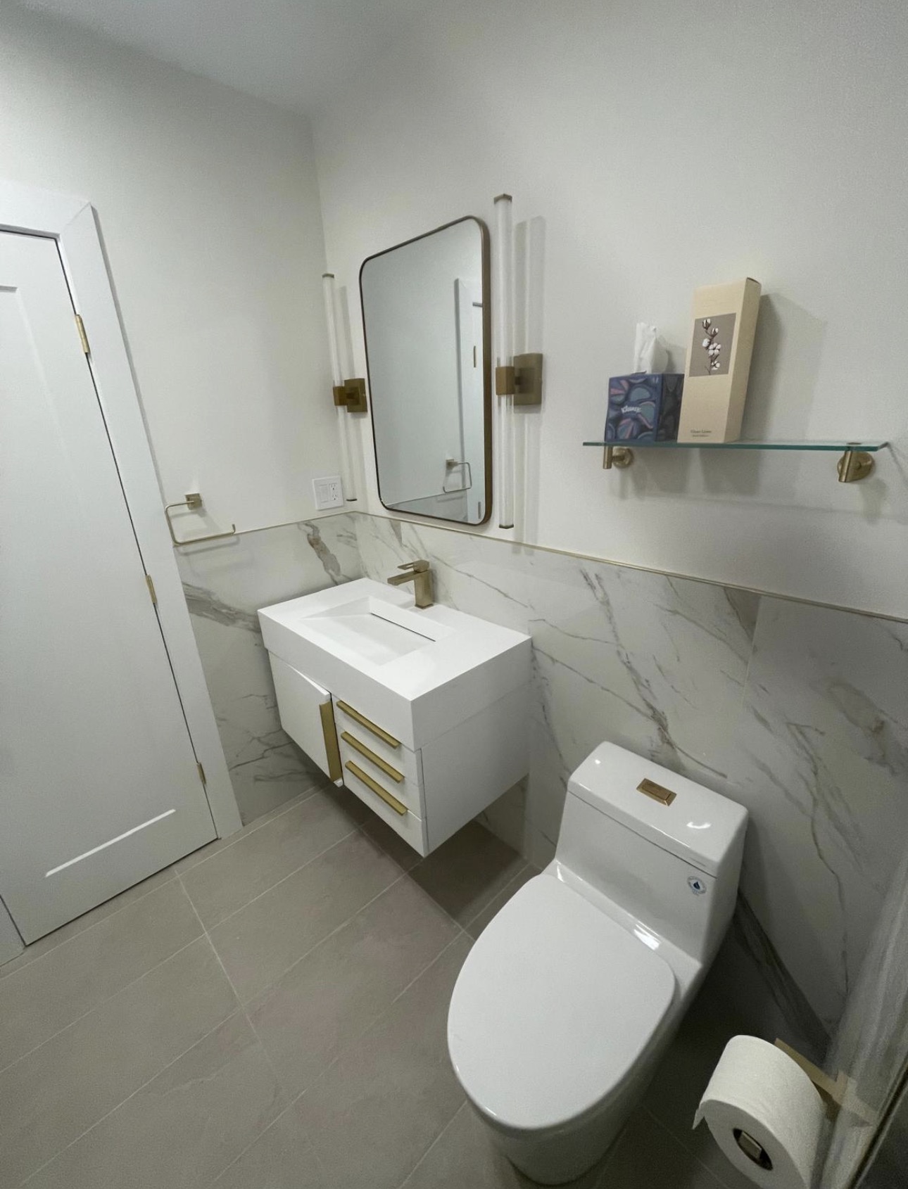 Powder bathroom with a floating white vanity, gold hardware, marble wainscot, and brass sconces