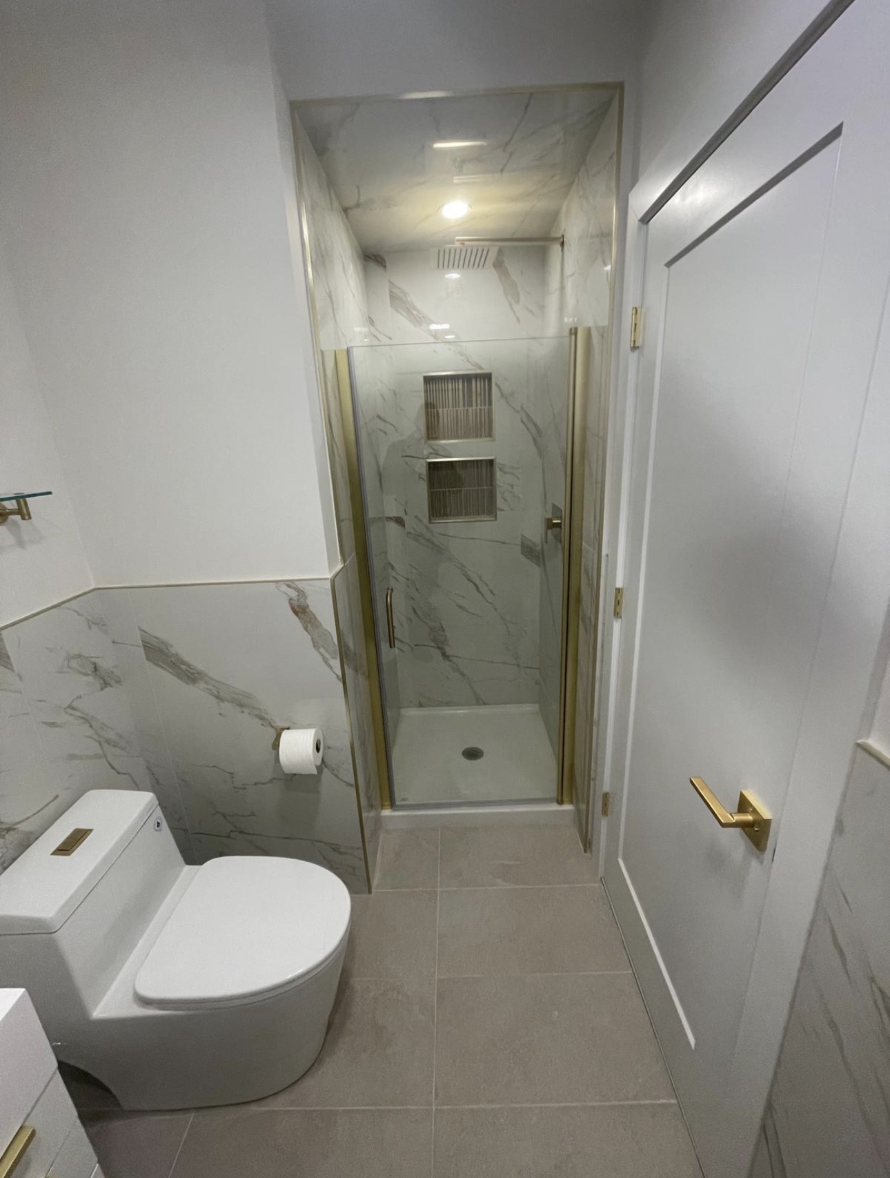 Marble wainscot bathroom with a gold-framed glass shower and dual niches
