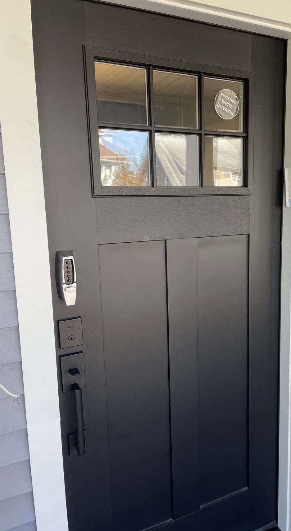 New black 6-lite exterior door with a smart lock, set in gray siding