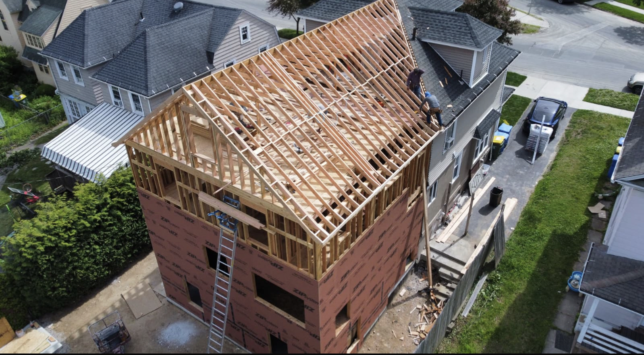 Aerial view of a Glazer Construction job site: a house with a new shingle roof and sheathed rear addition