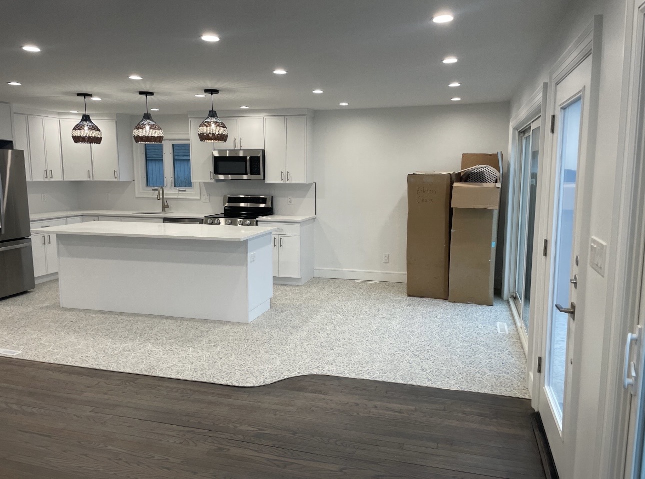 Finished kitchen with white cabinets, quartz island, pendant lights and hardwood flooring