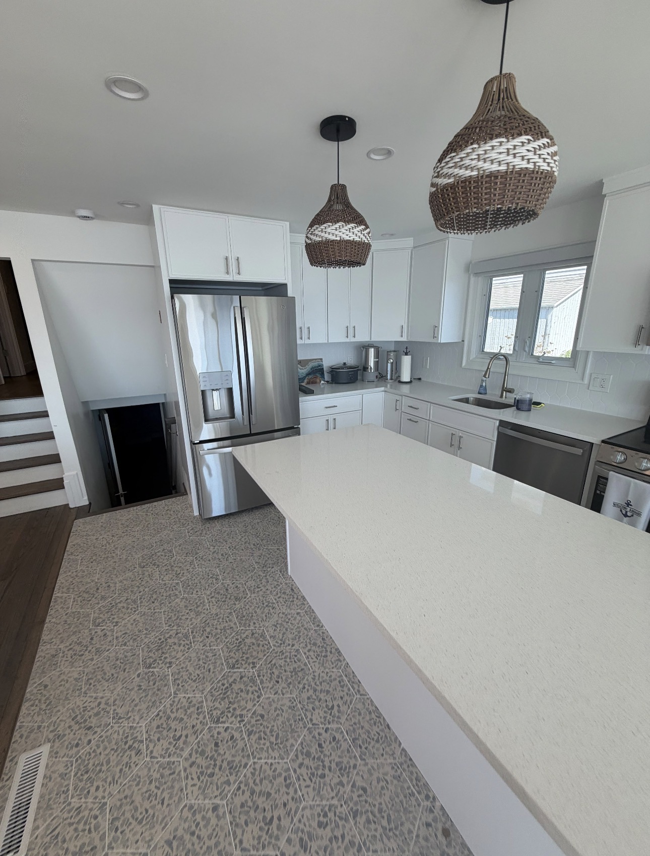 Kitchen with white cabinets, quartz island, woven pendant lights and hexagonal tile floor