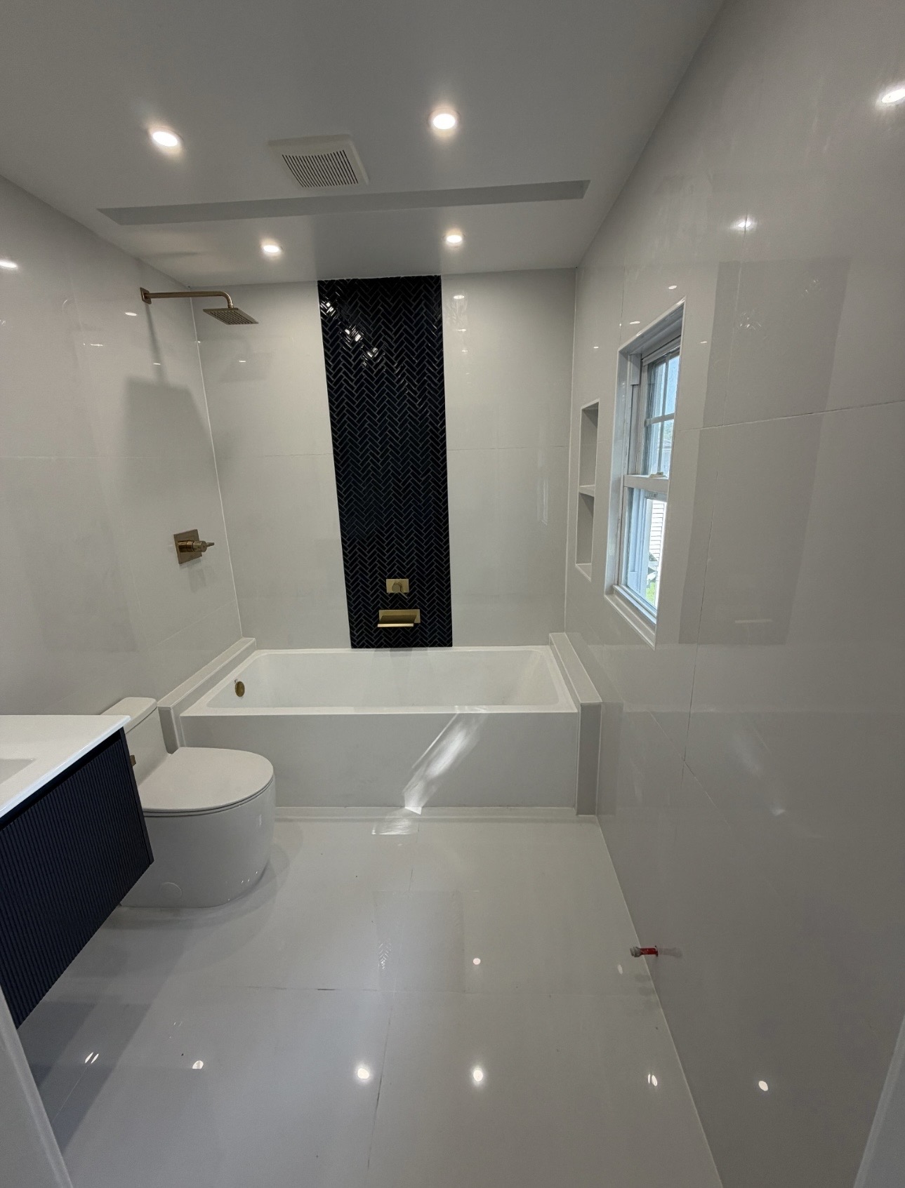 Finished master bathroom: large-format white tile, soaking tub, brass fixtures and a navy vanity