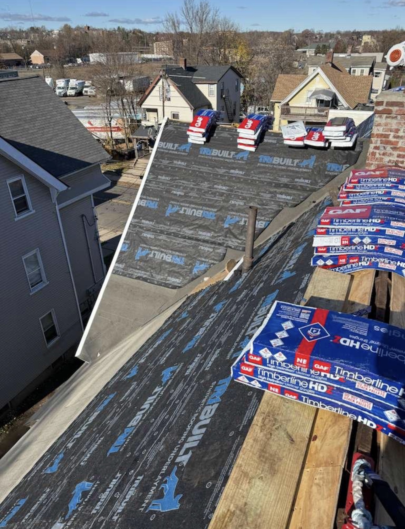 TRI-BUILT underlayment and GAF Timberline HD shingle bundles staged on a roof
