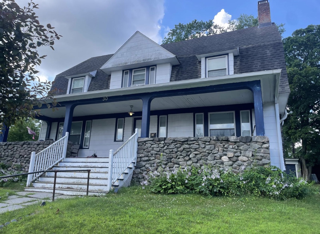 White clapboard house with navy porch columns, wraparound porch, and a stone foundation
