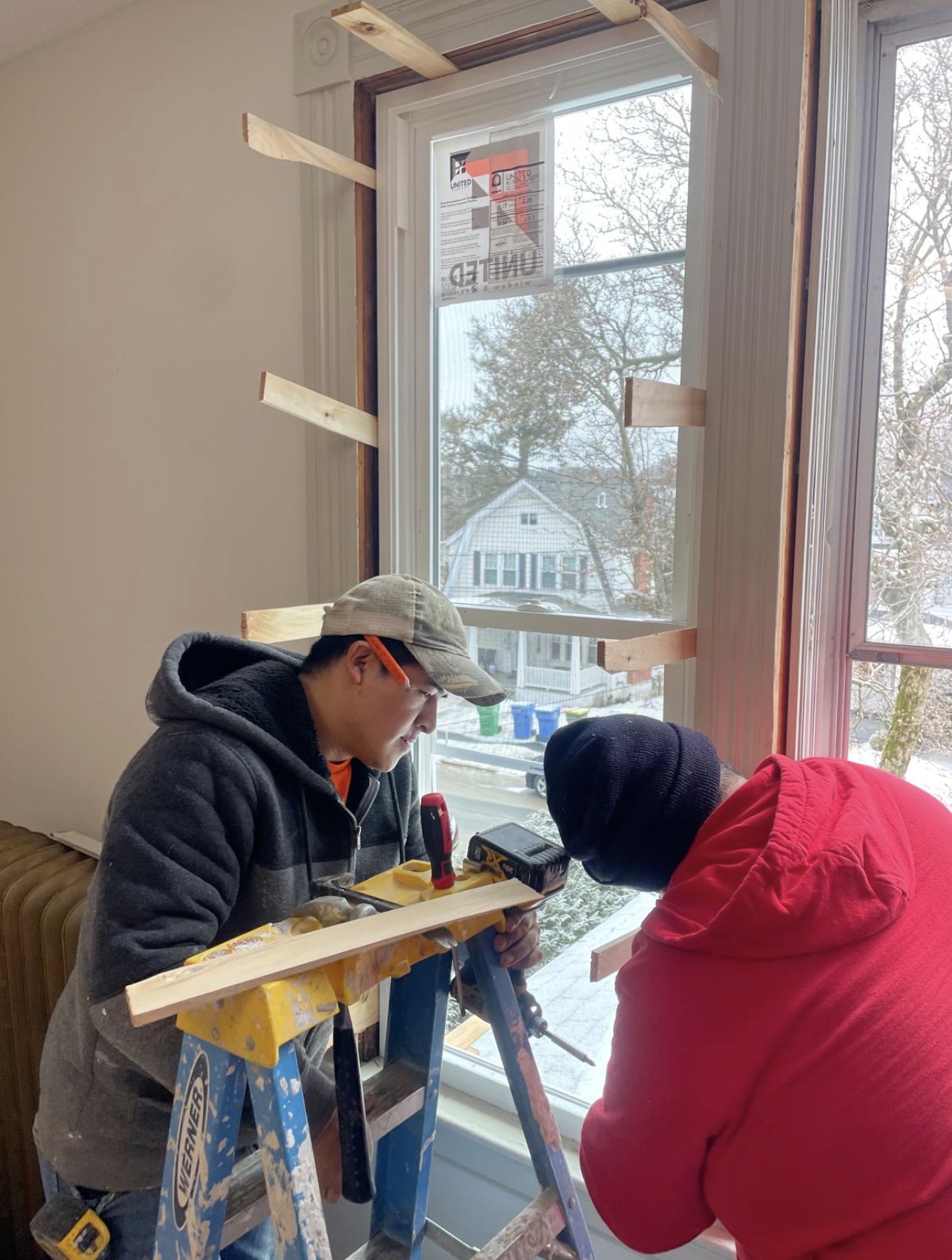 Two carpenters setting a replacement window, with shims holding the frame